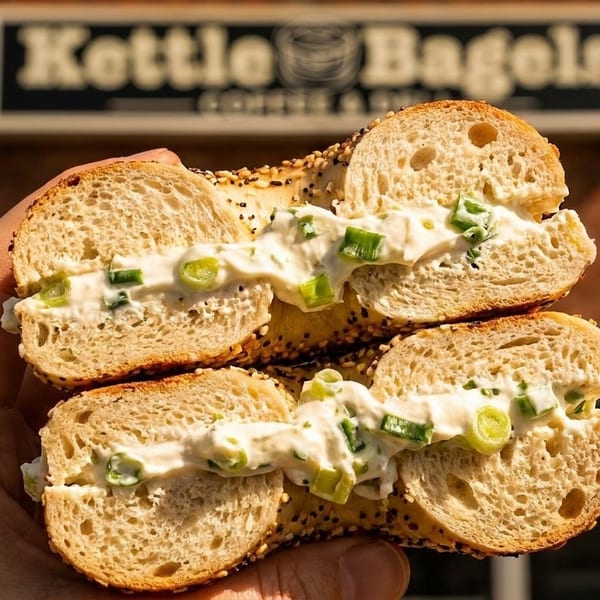 Hand holding a Kettle Bagels sesame bagel with scallion cream cheese, outside the shop.