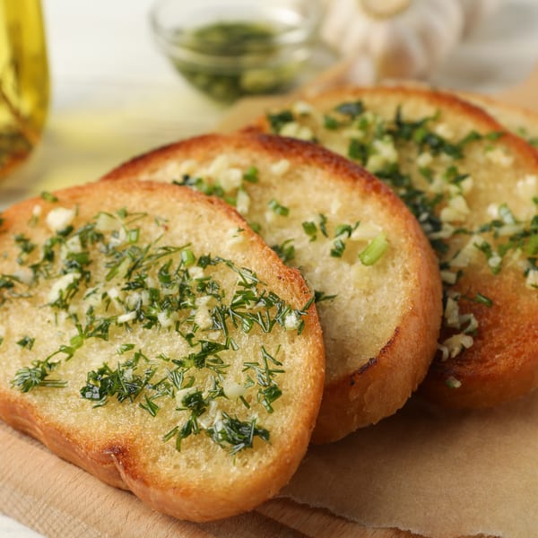 Four slices of golden-brown garlic bread topped with fresh herbs on a wooden board.