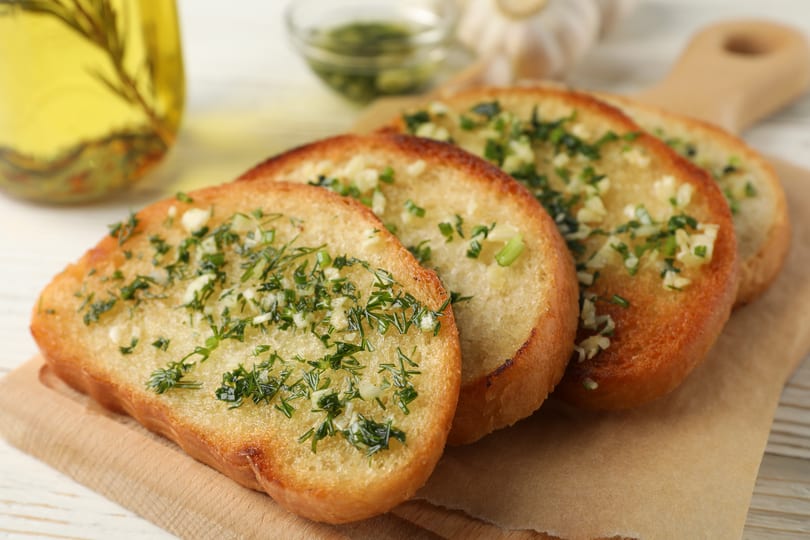 Four slices of golden-brown garlic bread topped with fresh herbs on a wooden board.