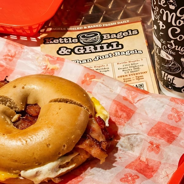 A Kettle Bagels & Grill breakfast sandwich with bacon, egg, and cheese, next to a coffee cup.
