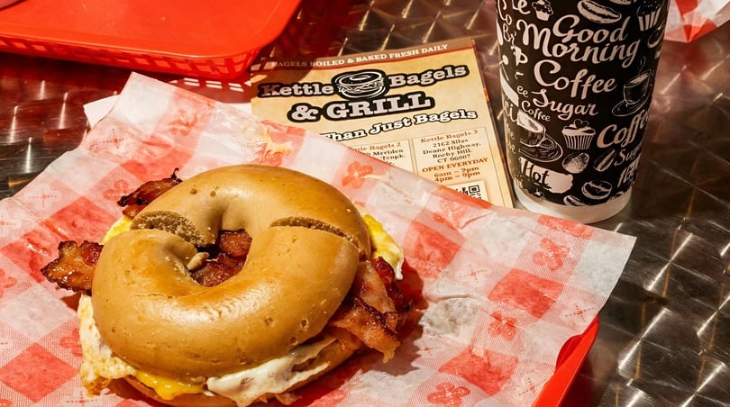 A Kettle Bagels & Grill breakfast sandwich with bacon, egg, and cheese, next to a coffee cup.