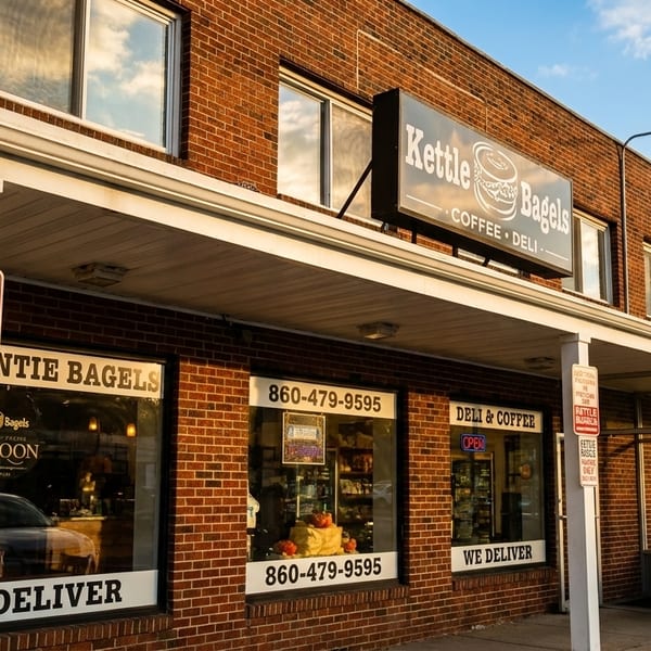 Exterior of Kettle Bagels, a brick building with a sign, windows, and parking signs under a blue sky.