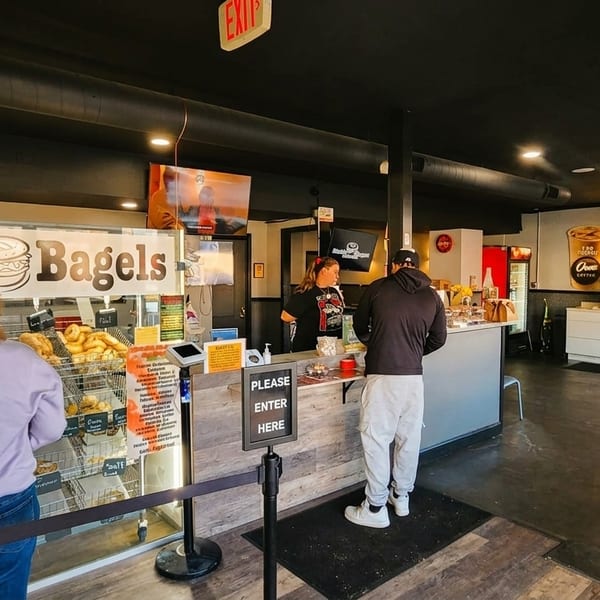 Customers ordering at the counter of Kettle Bagels, with a display of bagels and coffee station.