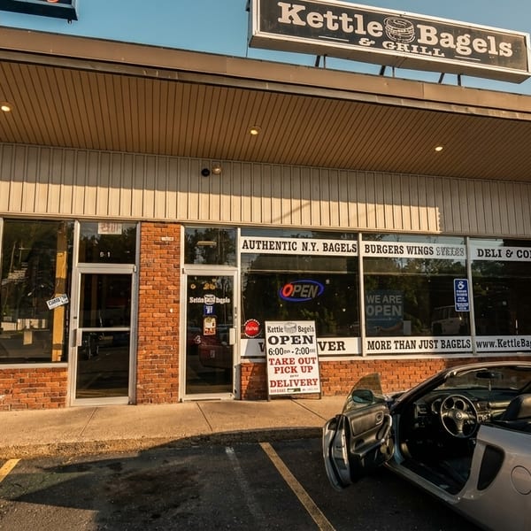 Exterior of Kettle Bagels & Grill with a silver convertible parked in front.