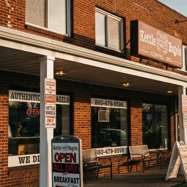 Exterior of Kettle Bagels, a brick building with a brown sign, windows, and an "Open All Day" sign.