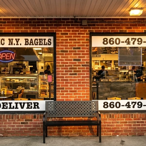 Exterior of a brick bagel shop with large windows, an "OPEN" sign, and a delivery number.