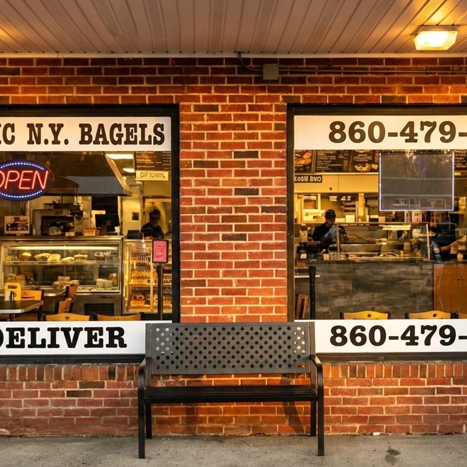Exterior of a brick bagel shop with large windows, an "OPEN" sign, and a delivery number.