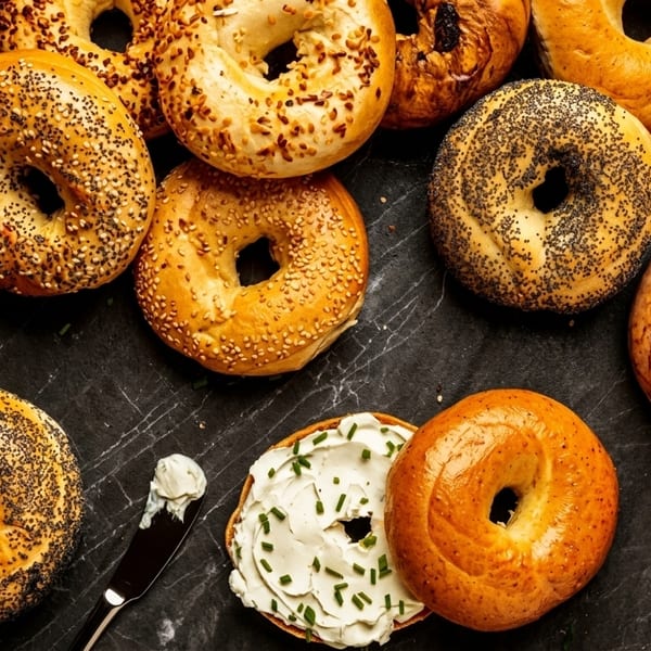 Assortment of bagels with various toppings, one with cream cheese and chives, on a dark surface.