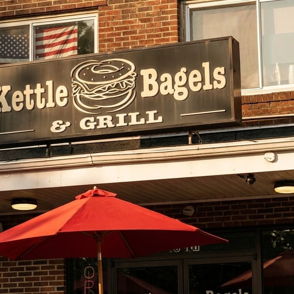 Kettle Bagels & Grill sign on a brick building with red umbrellas and an American flag in the window.