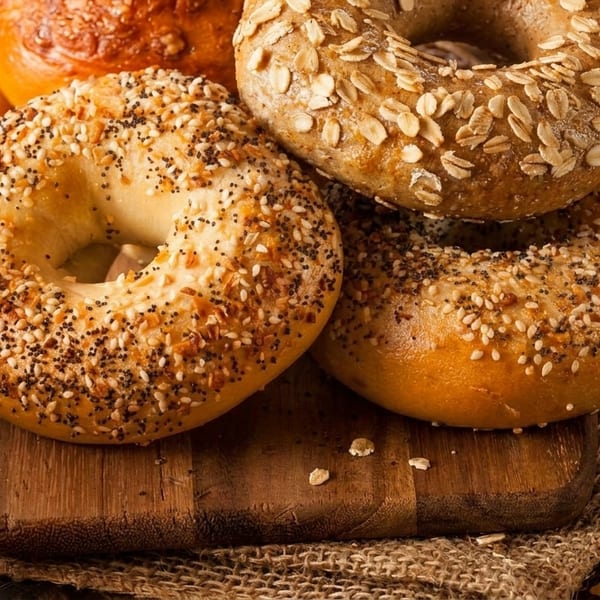 Assortment of fresh bagels, including plain, everything, and oat-topped, on a wooden board.